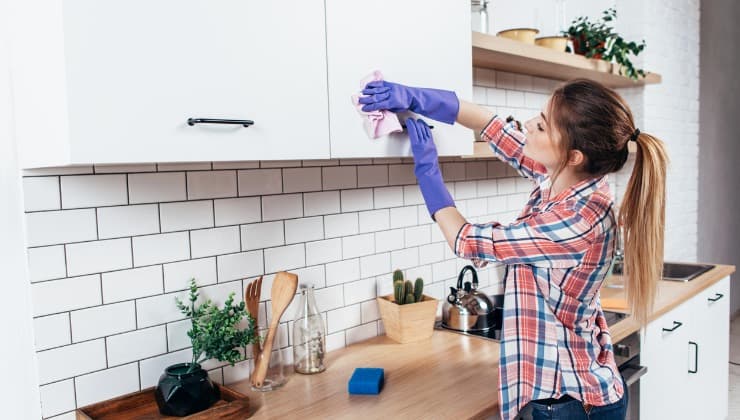 Donna pulisce grasso dai mobili della cucina